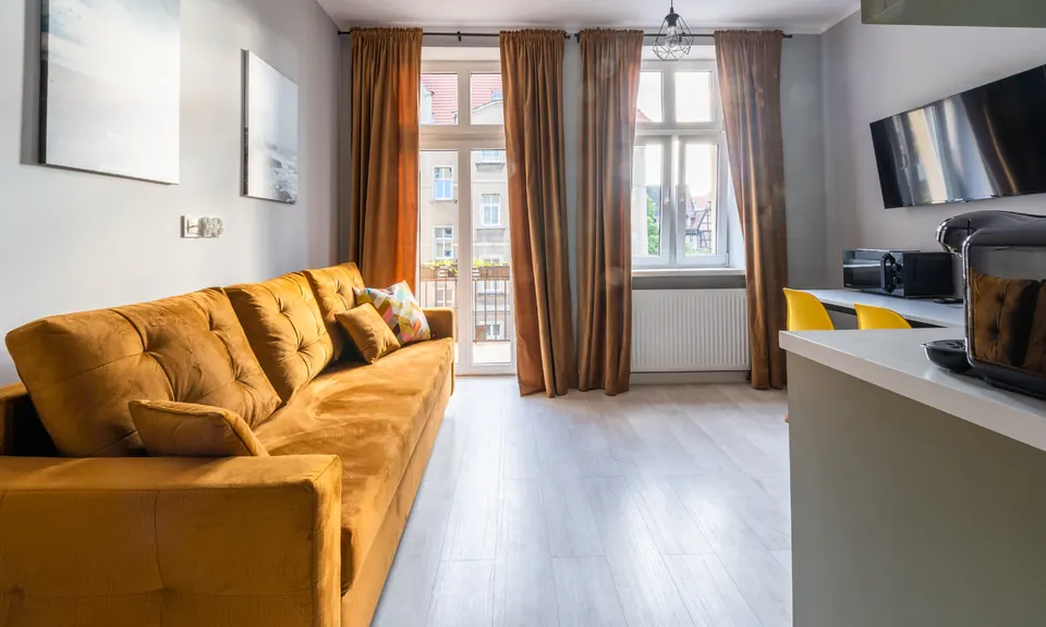 Studio z musztardową sofą i drzwiami na balkon