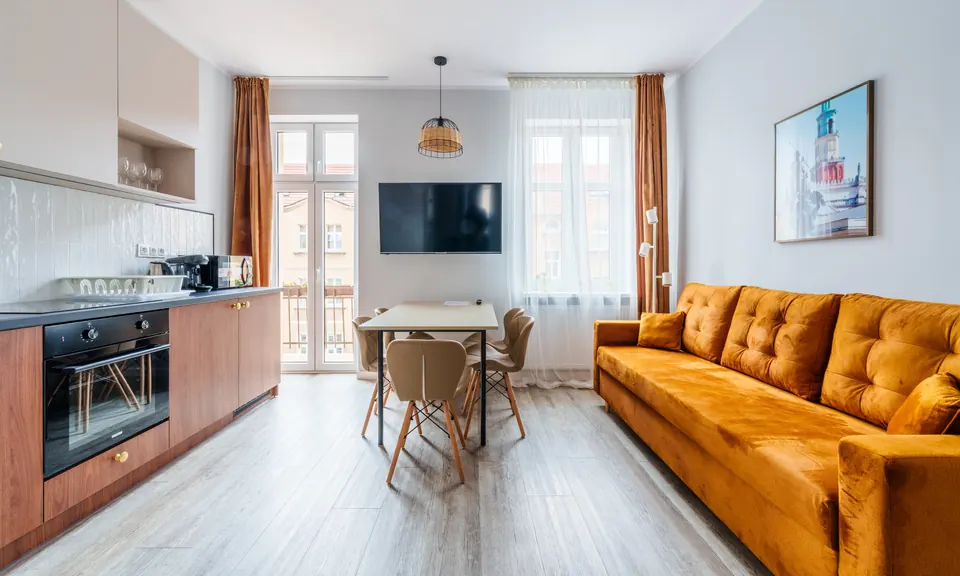 Salon z aneksem kuchennym, stołem i musztardową sofą