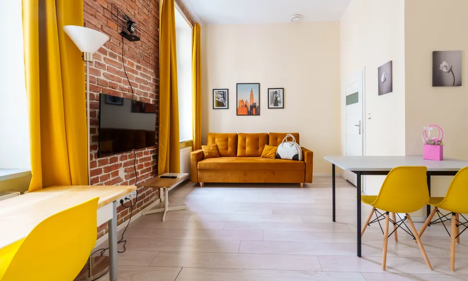 Studio z ceglaną ścianą, musztardową sofą i stołem
